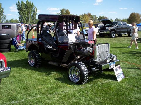 1972 Ford Ranchero - A heavily modified Jeep CJ is displayed at an outdoor car show, with other vehicles and attendees in the background.