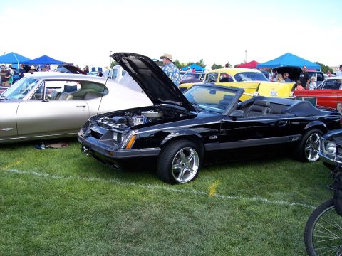 1972 Ford Ranchero - A black convertible with its hood open sits on a grassy field next to other vehicles.
