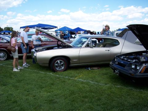 1972 Ford Ranchero - A gold 1969 Pontiac Grand Prix is displayed with its hood up at an outdoor car show.
