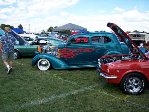 1972 Ford Ranchero - A teal hot rod with flame decals and a custom engine sits on display at a car show.