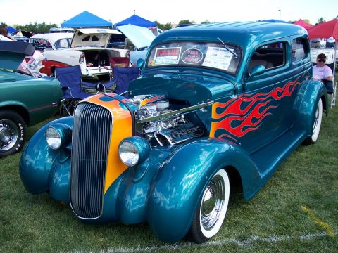 1972 Ford Ranchero - A teal hot rod with flame decals and an exposed engine is displayed on a grassy field, with other vehicles and tents in the background.