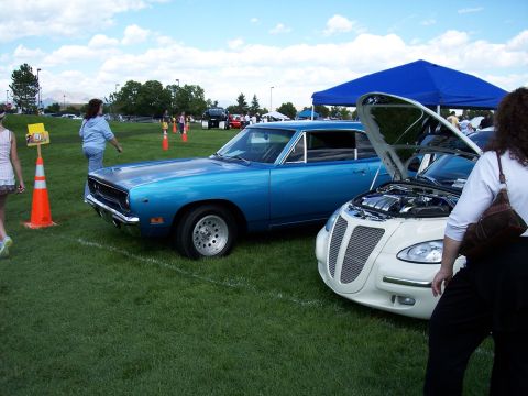 1972 Ford Ranchero - A blue 1970s muscle car is displayed at an outdoor car show next to a white modern vehicle with its hood open.