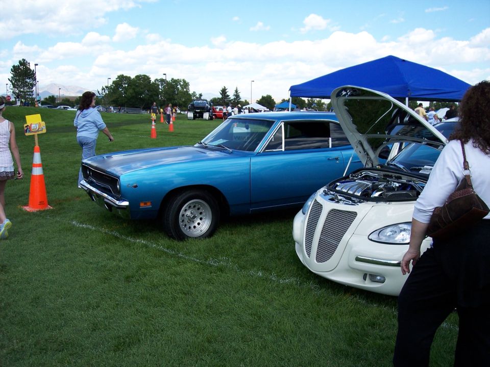 Blue 1970s muscle car parked next to a white modern car with hood open