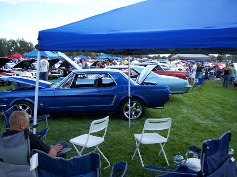 1972 Ford Ranchero - A blue 1965 Ford Mustang coupe is displayed under a blue canopy at an outdoor car show.