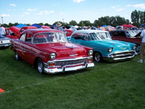 1972 Ford Ranchero - Two vintage Chevrolet sedans are displayed on a grassy field under a partly cloudy sky at an outdoor car show.