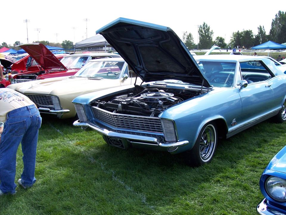 Blue 1967 Buick Riviera coupe with hood open, showing engine. Parked on grass at car show