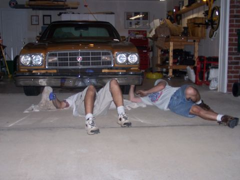 1973 Ford Ranchero - Two men work on the underside of a gold 1977 Ford Ranchero in a garage.