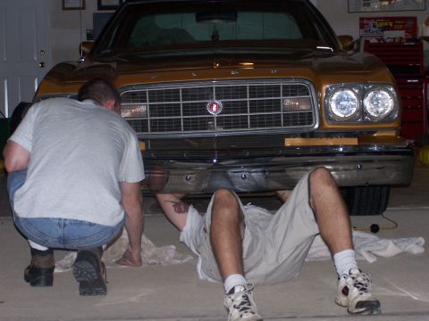 1973 Ford Ranchero - Two men work on the front bumper and grille of a gold 1973 Ford Ranchero in a garage.