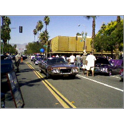2007 Ford Ranchero - A street scene with multiple classic cars and onlookers on a sunny day.