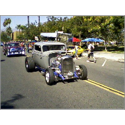 2007 Ford Ranchero - A custom hot rod with a prominent engine is shown on a street, with other vehicles and pedestrians present.