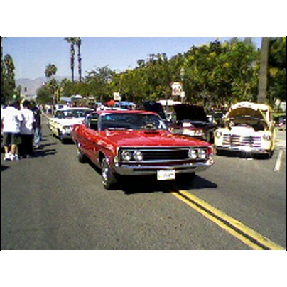 2007 Ford Ranchero - A red convertible is parked on a street with other vehicles and spectators.