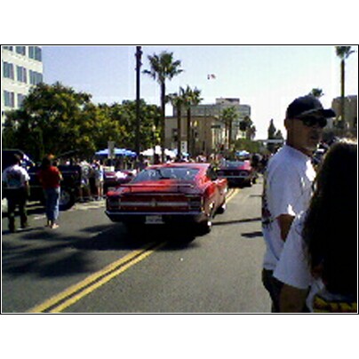 2007 Ford Ranchero - A red 1968 Ford Ranchero is seen driving in a parade or car show, with other vehicles and spectators present.