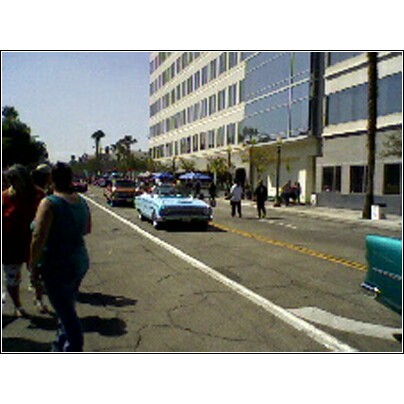 2007 Ford Ranchero - A blue convertible cruises down a street lined with buildings and spectators.