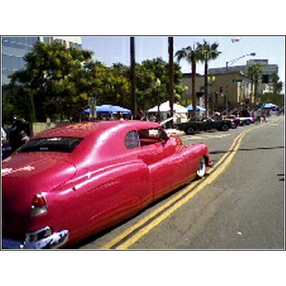 2007 Ford Ranchero - A line of cars are parked along a street with buildings and palm trees in the background.