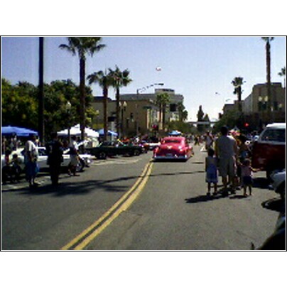 2007 Ford Ranchero - A red classic car drives down a street during a parade, with palm trees and buildings lining the route.