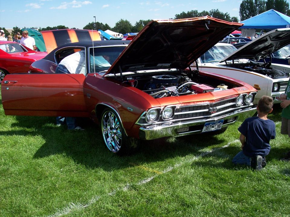 Orange 1969 Chevrolet Chevelle SS with hood and driver door open, parked on grass at car show