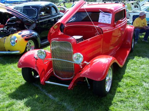 1972 Ford Ranchero - A red hot rod coupe is displayed at an outdoor car show, with other vehicles visible in the background.