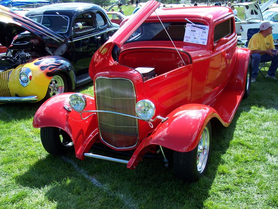 Red hot rod coupe with hood open, parked on grass next to a black car and a yellow car with flames
