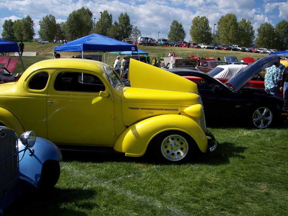 Yellow coupe with hood open, parked on grass at an outdoor car show