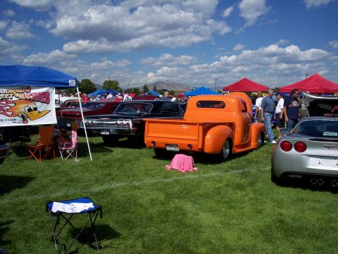1972 Ford Ranchero - An orange classic pickup truck is parked on the grass at a car show, with other vehicles and tents in the background.