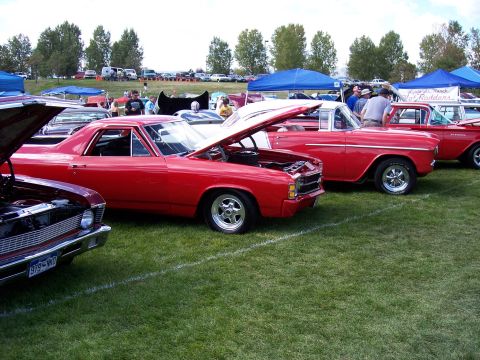 1972 Ford Ranchero - Several classic red cars are displayed on a grassy field under a bright sky.