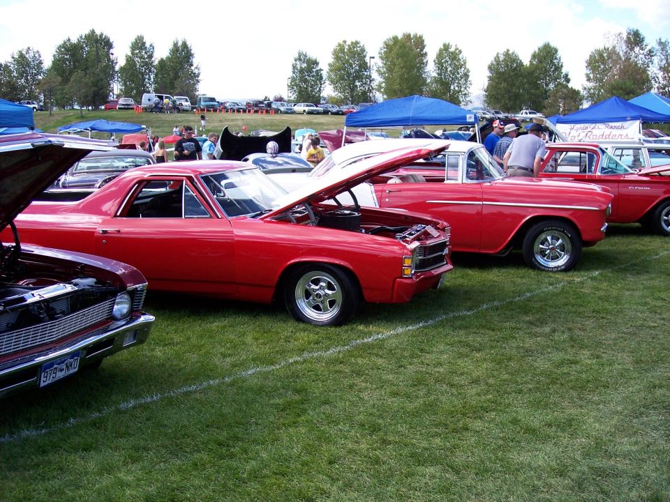Red 1970s era car with hood open, showing engine, parked on grass at a car show
