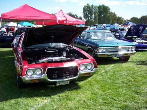 1972 Ford Ranchero - Red 1970s pickup truck and a green 1960s car at an outdoor car show.