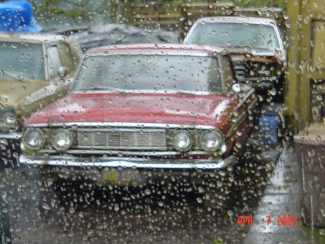 Red vintage Ford sedan front view seen through rainy glass