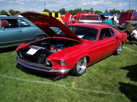 1972 Ford Ranchero - A red 1969 Ford Mustang Mach 1 is displayed with its hood open at an outdoor car show on a sunny day.