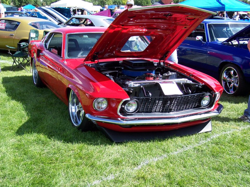 Red 1969 Ford Mustang coupe with hood open, showing engine, parked on grass