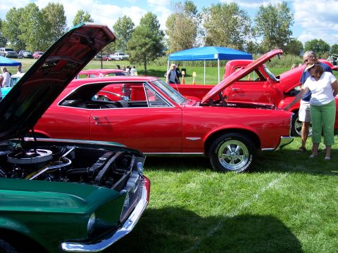 1972 Ford Ranchero - Two classic cars, a red coupe and a green car, are displayed with their hoods open at an outdoor event.