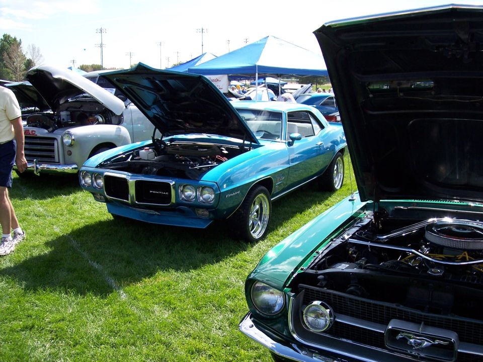 Blue 1969 Pontiac Firebird with hood open, parked on grass next to a green Ford Mustang