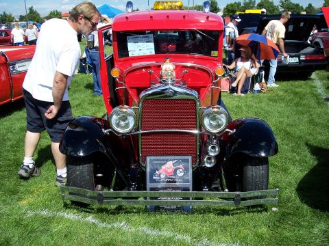 1972 Ford Ranchero - A vintage red truck is displayed on a grassy field at an outdoor event, with spectators around.