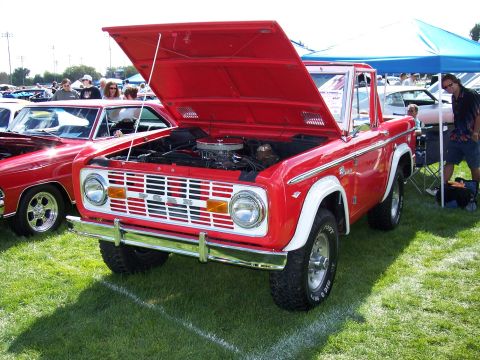 1972 Ford Ranchero - A red Ford Bronco is displayed with its hood open at an outdoor event, parked next to another vehicle.