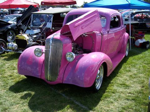 1972 Ford Ranchero - A custom pink hot rod is displayed with its hood open at an outdoor car show.