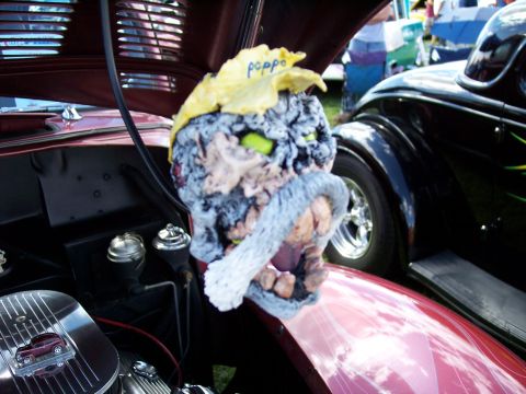 1972 Ford Ranchero - A quirky, monster-like hood ornament sits atop a car's engine bay at an outdoor car show.