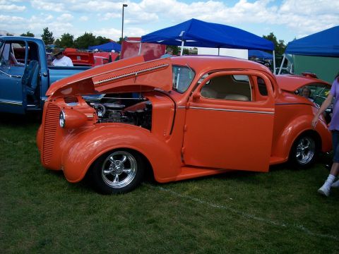 1972 Ford Ranchero - An orange coupe with its hood and door open sits on a grassy field at an outdoor event.