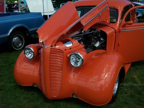 1972 Ford Ranchero - An orange hot rod with its hood and door open sits on grass next to a blue pickup truck.
