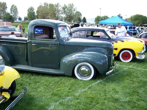 1972 Ford Ranchero - A vintage green pickup truck is displayed at an outdoor car show alongside other classic vehicles.