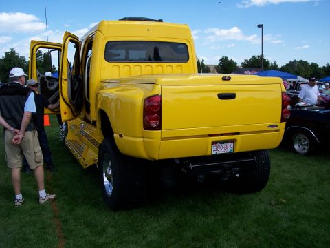 1972 Ford Ranchero - A bright yellow custom dually pickup truck is parked on a grassy field with its doors open.