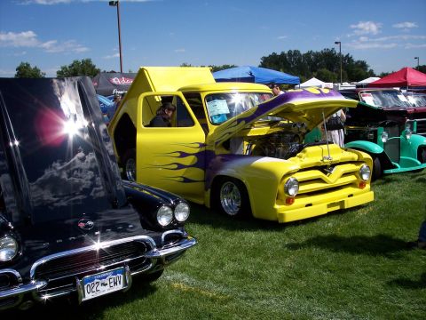 1972 Ford Ranchero - A customized yellow pickup truck with purple flame graphics and an exposed engine is displayed at an outdoor car show.