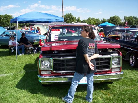 1972 Ford Ranchero - A red pickup truck is displayed at an outdoor car show with a woman posing in front of it.