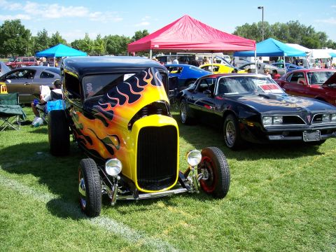 1972 Ford Ranchero - Outdoor car show features a flame-painted hot rod and a black Pontiac Trans Am.