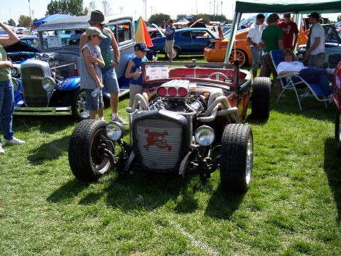 1972 Ford Ranchero - A custom hot rod with a prominent skull emblem on its grille is displayed at an outdoor car show with other vehicles and attendees.