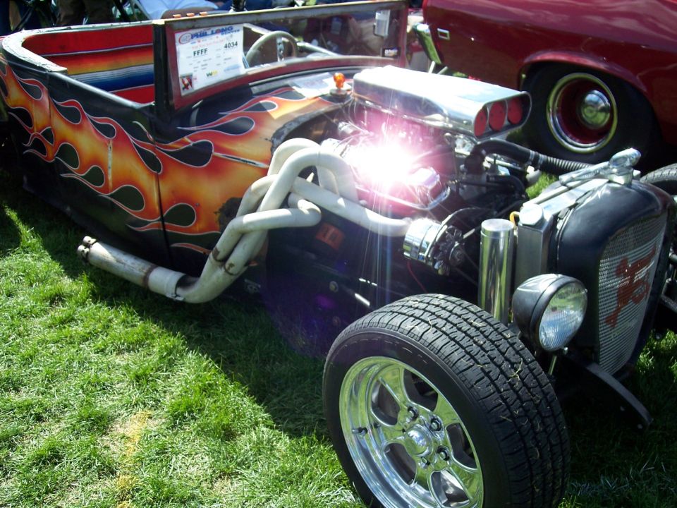 Hot rod with flame paint, exposed engine, and chrome wheels. Another car is visible to the right