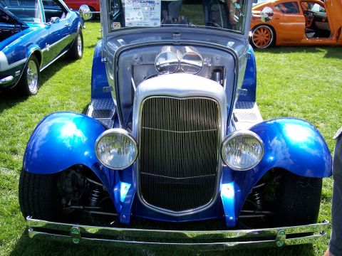 1972 Ford Ranchero - A blue hot rod with a prominent chrome grille and dual carburetors is parked on grass next to other vehicles.