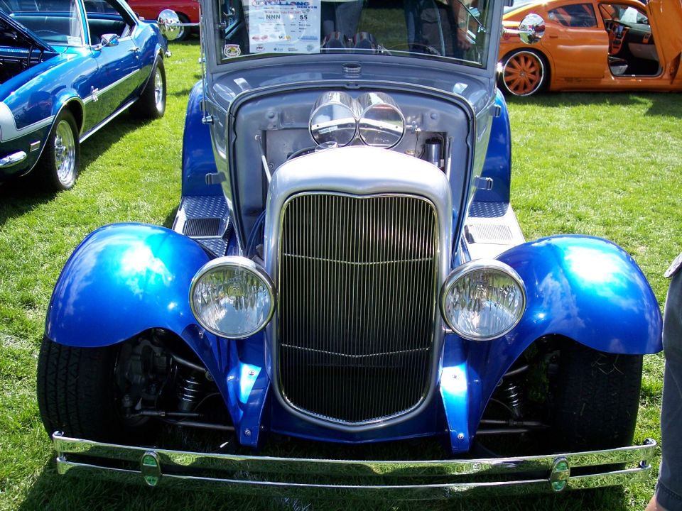 Blue hot rod with chrome grille and dual carburetors. Visible text on windshield