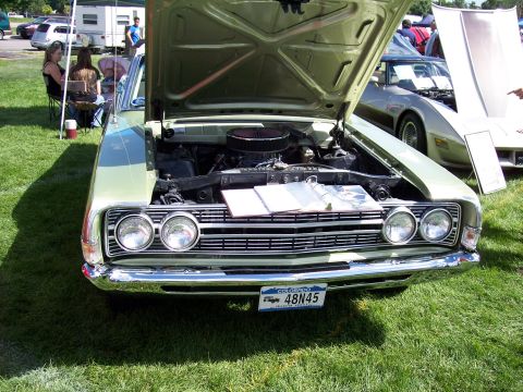 1972 Ford Ranchero - A light green 1970s coupe is displayed with its hood open, revealing the engine and a brochure. Another vehicle is visible in the backgroun…