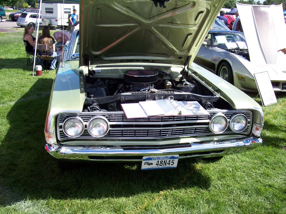 Light green 1970s coupe front view, hood open, showing engine and a brochure on display. Colorado license plate 48N45