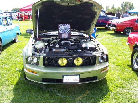 1972 Ford Ranchero - A light green Ford Mustang is displayed with its hood open at an outdoor car show, revealing the engine bay.